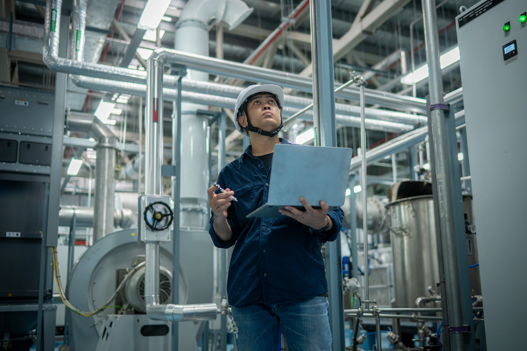 Engineer inspecting industrial machinery with clipboard in factory setting.